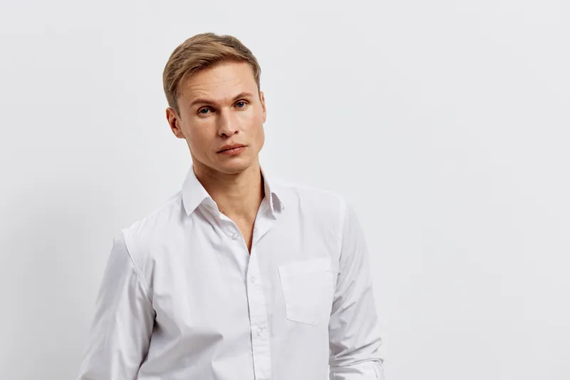 Professional studio portrait of a young man with blonde hair and fair skin wearing a white shirt, looking confidently at the camera isolated on a plain white background. Casual business style, lifesty