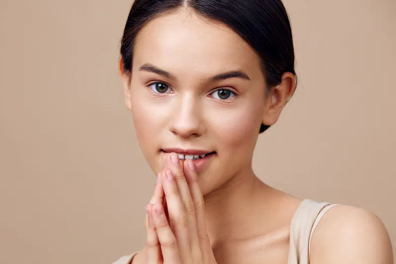Young woman expressing joy and serenity with gentle facial expression, neutral background highlighting natural beauty and simplicity in portrait photography