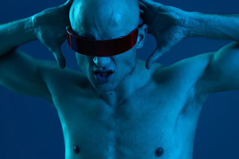 A striking image of a man with futuristic glasses, expressing intense emotions against a blue background. The captivating colors create a bold visual impact.