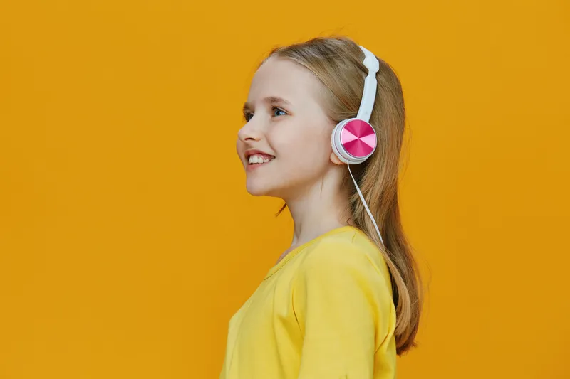 Cheerful girl listening to music with pink headphones against a vibrant yellow background, showcasing joy and creativity in a bright, playful setting