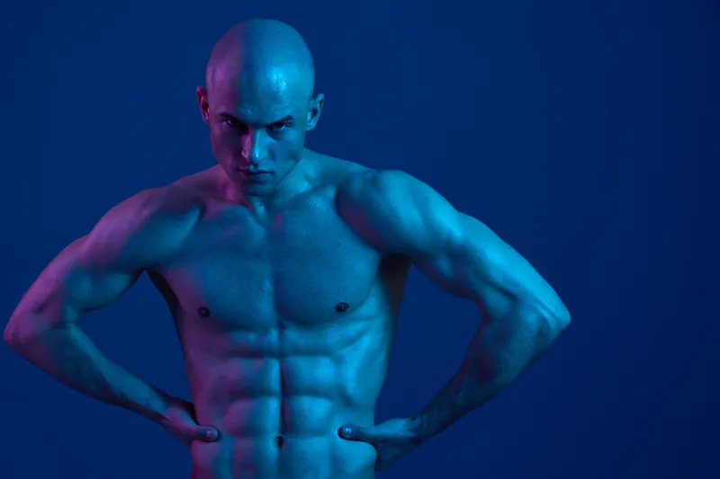 Strong man posing with confidence, showcasing well-defined muscles in a dramatic blue and violet lighting. Emphasizes strength and determination in a unique style.