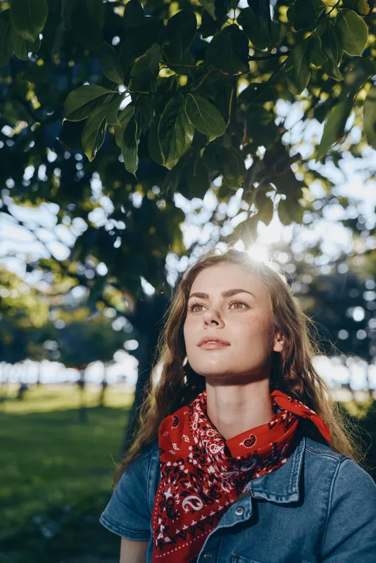 Lifestyle woman in modern boho-western denim street style with a red bandana, natural sunlight, and film color tone creating a warm, relaxed outdoor atmosphere.