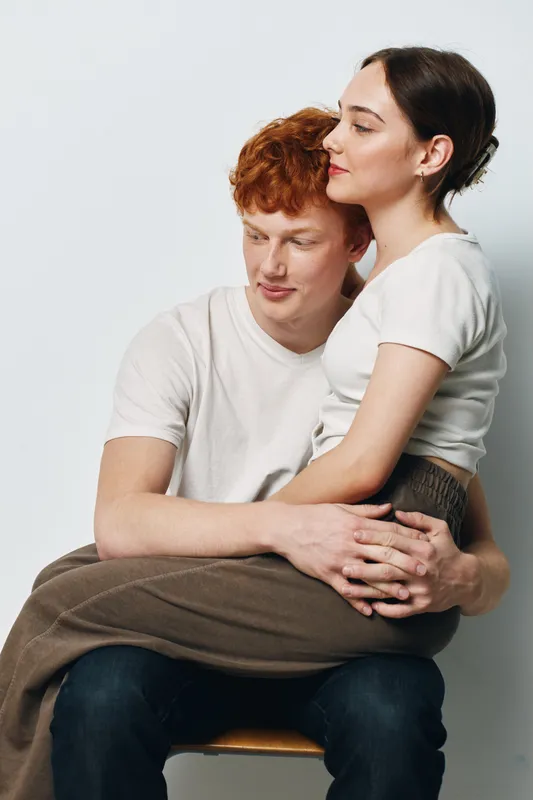 Couple, woman and man embracing with affection and love while sitting together. Young people showing intimacy, connection and warmth in casual clothing on plain background.
