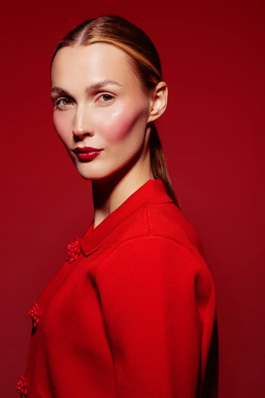 Portrait of a woman with red lipstick and blush wearing a red sweater against a red background. Concept of fashion, beauty, and monochrome style with strong color contrast.
