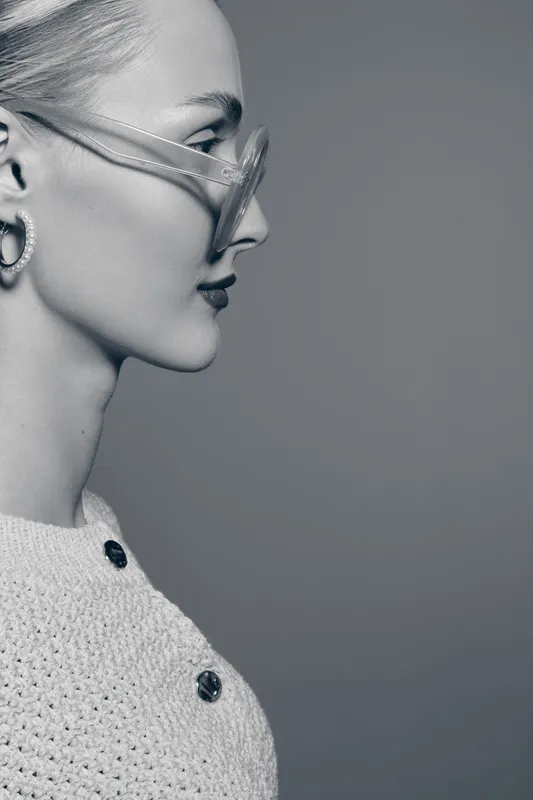 Profile of a young Caucasian woman with pale skin wearing transparent glasses and knitwear. Concept of fashion, style, and modern accessories in studio.