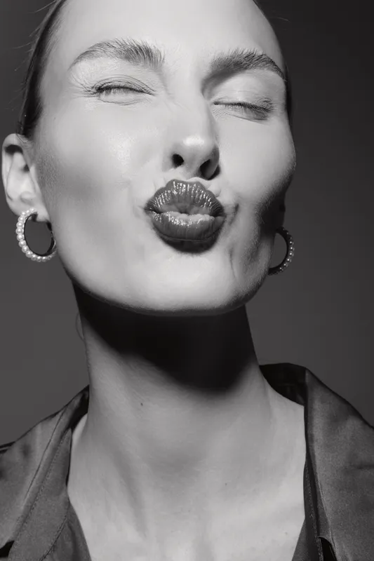Young caucasian woman with fair skin puckers lips for a kiss, eyes closed. Black and white portrait with hoop earrings and smooth skin, concept for beauty, emotion, and affection.