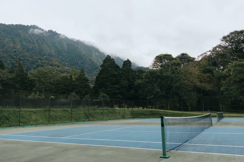 Serene tennis court in the mountains with misty background, featuring calming blue colors for a refreshing and tranquil atmosphere