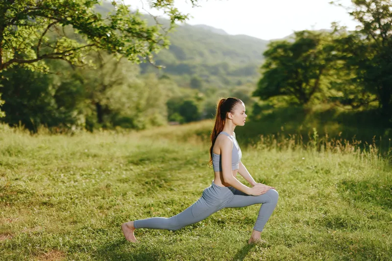 Young woman practicing yoga in a serene green field, wearing grey athletic wear and reflecting tranquility, embodying wellness and fitness in nature