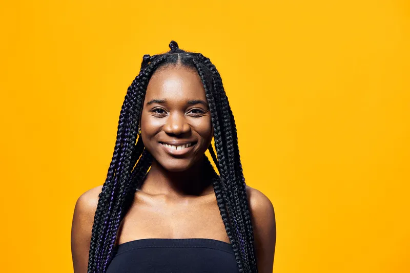 Smiling young woman with braided hair against a bright yellow background, perfect for showcasing confidence and positivity in lifestyle imagery