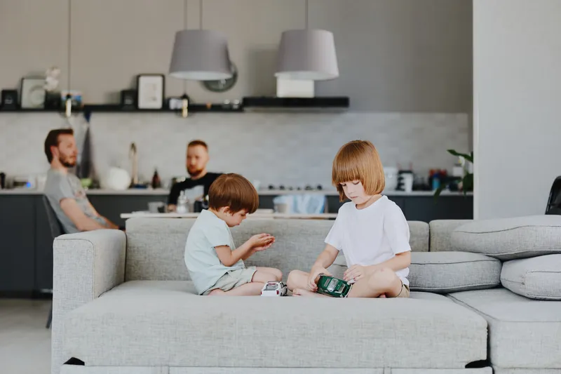 Playful children enjoying a cozy moment at home, surrounded by family. A boy and a girl sit on the sofa engaged in creative play, showcasing joy and togetherness. ###