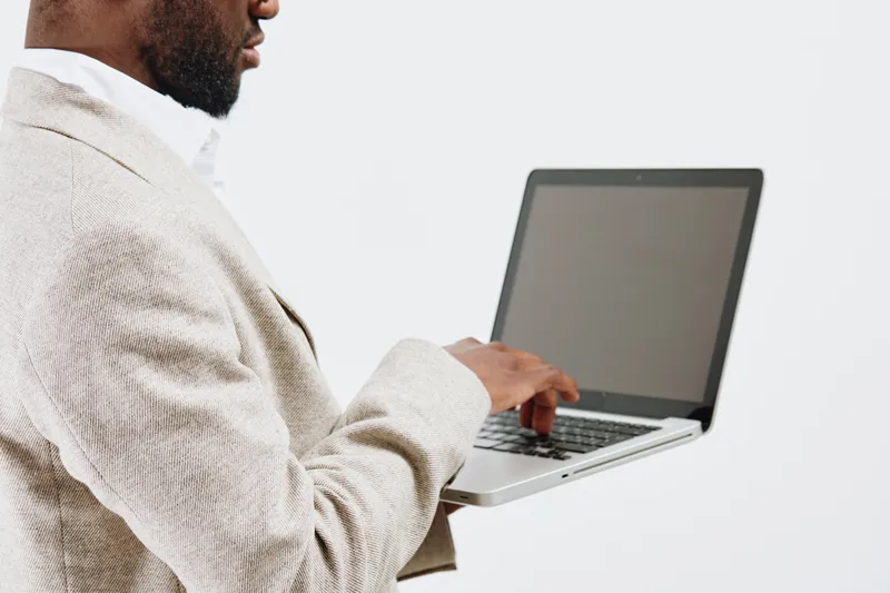 Modern man holding laptop computer in hand, wearing beige sweater, close-up of upper body, indoor shot, neutral background. Business technology, work, electronics, professional, contemporary style, ca