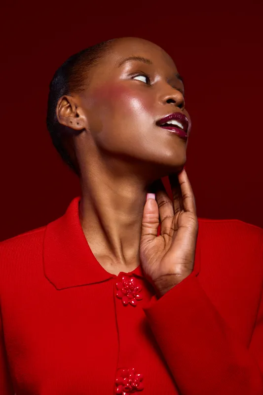 Portrait of a dark skinned African American woman in red clothing looking sideways. Studio shot with deep red background. Concept for beauty, fashion, and elegance with glossy makeup.