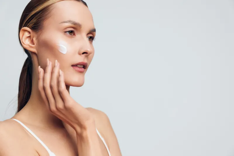 A woman applies cream to her cheek in profile, emphasizing skincare routine and self care. A calm, intimate beauty moment captured in natural light.