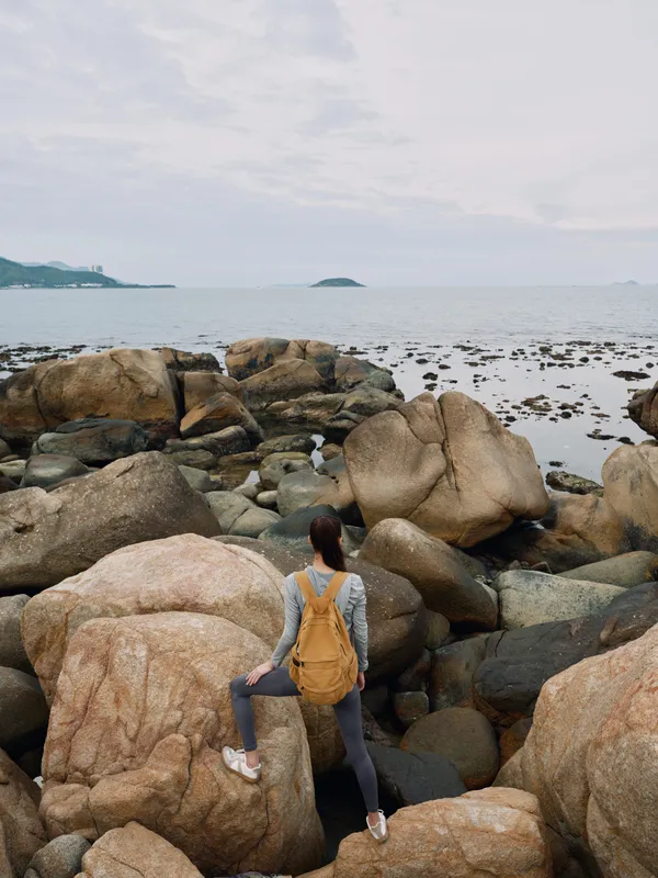 Young woman in athletic wear exploring rocky coastal scenery, showcasing adventure, nature, and fitness with a serene ocean backdrop