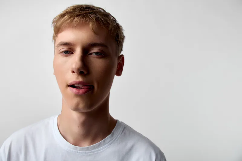Young man in a white tshirt offers a relaxed headshot in a studio with a neutral background, showcasing natural mood, facial expression and clean lighting