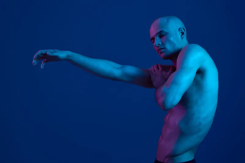 Male model with artistic pose, showcasing emotions in a striking blue light environment. The image captures a unique blend of creativity and expression.