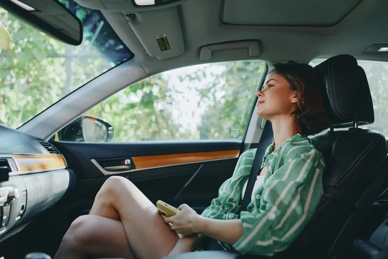 a young woman sits in the driver's seat of a car, relaxed and smiling, ready for a journey
