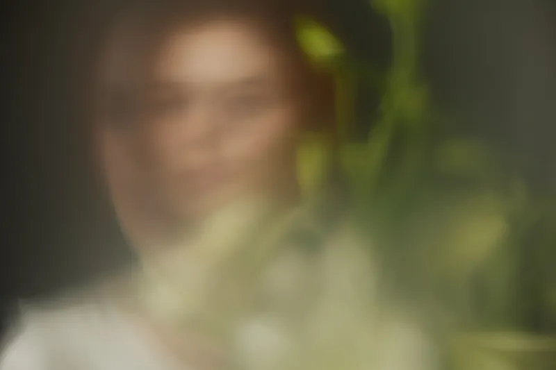 Ethereal portrait of a woman with blurred foliage, embodying serenity and natural beauty, ideal for wellness and lifestyle themes
