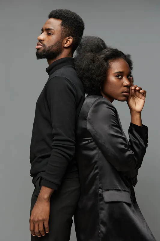 Stylish African couple standing back to back, expressing confidence and individuality in modern fashion against a minimalist gray background