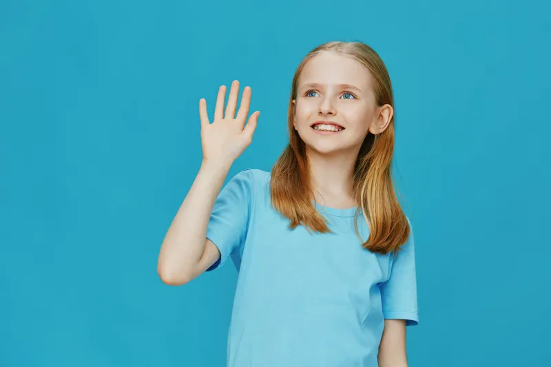 Happy young girl waving on a bright blue background, wearing a light blue shirt, showcasing joy and innocence Perfect for children s themes and positive emotions