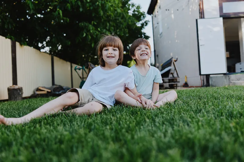 Happy children enjoying a sunny day outdoors, sitting on green grass, laughing and playing together, showcasing the joy of childhood friendship in a natural setting.