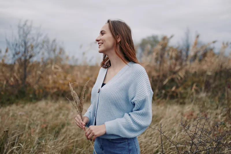 [Young woman smiling in a windswept field captured in an authentic, genuine moment of quiet joy; natural light and candid posture emphasize a real lifestyle portrait.]