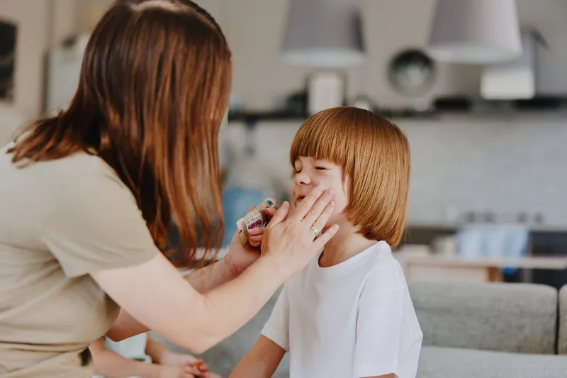 Caring woman applying makeup on her child in a cozy home environment, capturing a moment of love and tenderness between the two.