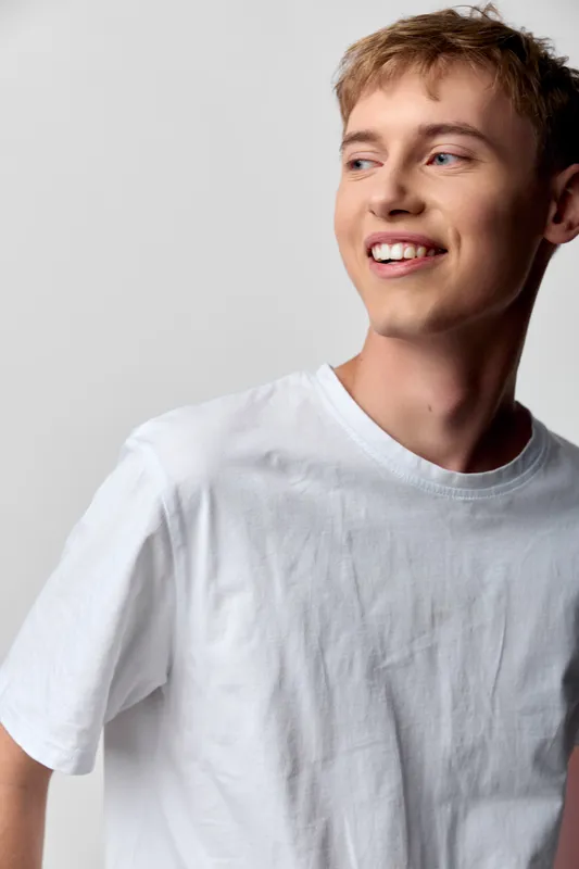 Young man smiling, casual white t shirt studio setting happiness fashion lifestyle style urban comfortable cheerful bright pleasant modern confident youth male expression candid natural relaxed pose