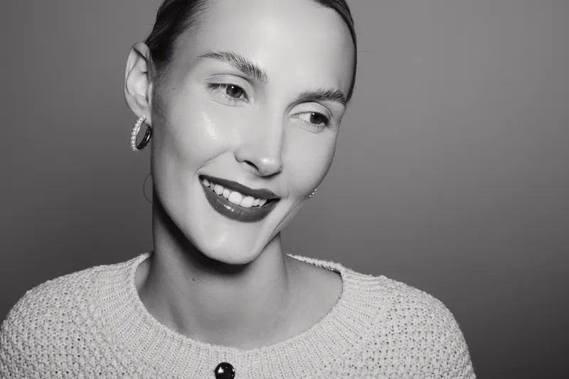 Smiling white woman with light skin and short hair in a knitted sweater looks aside in black and white portrait.
