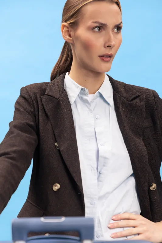Confident businesswoman in dark blazer and white shirt looks focused and determined against blue background. Concept for professionalism, leadership, office work, and corporate environment.