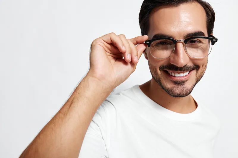 Smiling man wearing glasses and white t-shirt, looking at the camera with a cheerful expression, isolated on a plain solid background in a studio portrait.