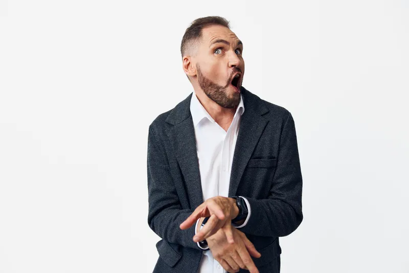 A professional man in business attire stands against a clean colored background, displaying a genuine surprise emotion. The image conveys energy, confidence, and dynamism for corporate, marketing, or