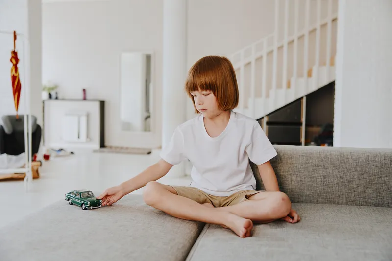 Playful boy enjoying a toy car in a bright, modern living room, showcasing creativity and childhood joy in a serene atmosphere.