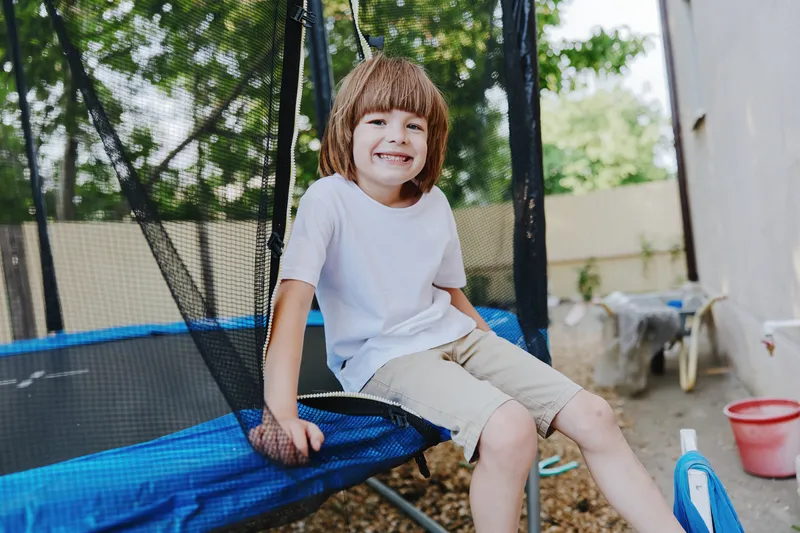 Smiling boy enjoying playful moments on a trampoline, surrounded by greenery and a cheerful atmosphere, perfect for capturing childhood joy and fun.