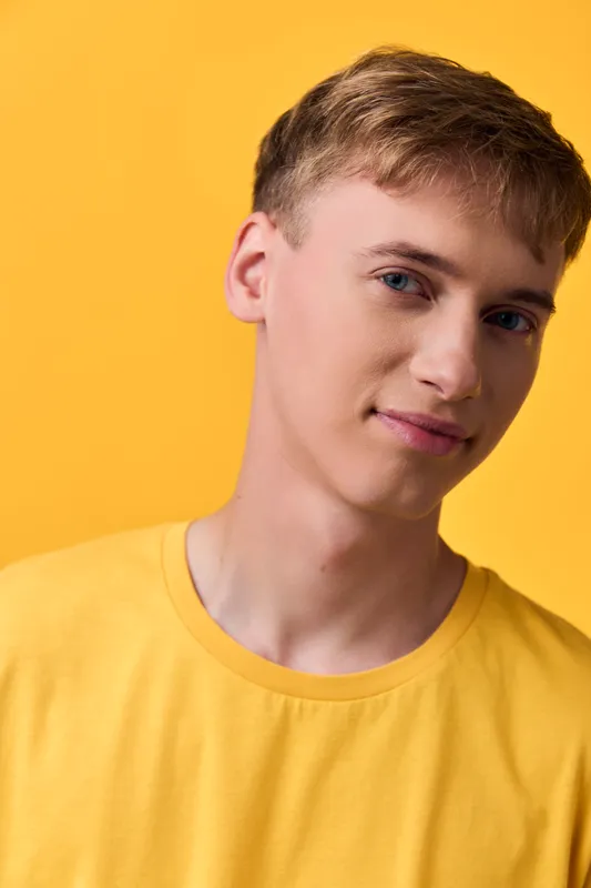 Young man in a yellow shirt poses against a vivid yellow backdrop, studio lighting highlighting clean features and a relaxed smile, casual mood perfect for lifestyle and fashion content