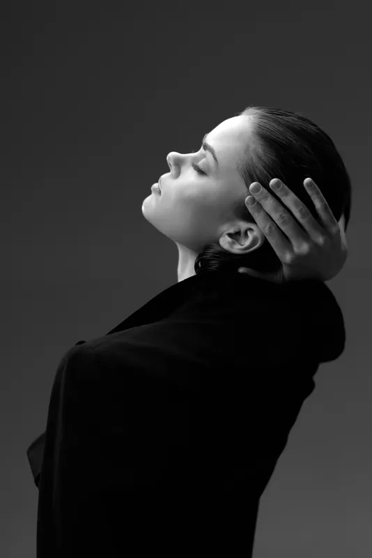 black and white profile portrait of a calm woman with closed eyes in dark clothing against gray background