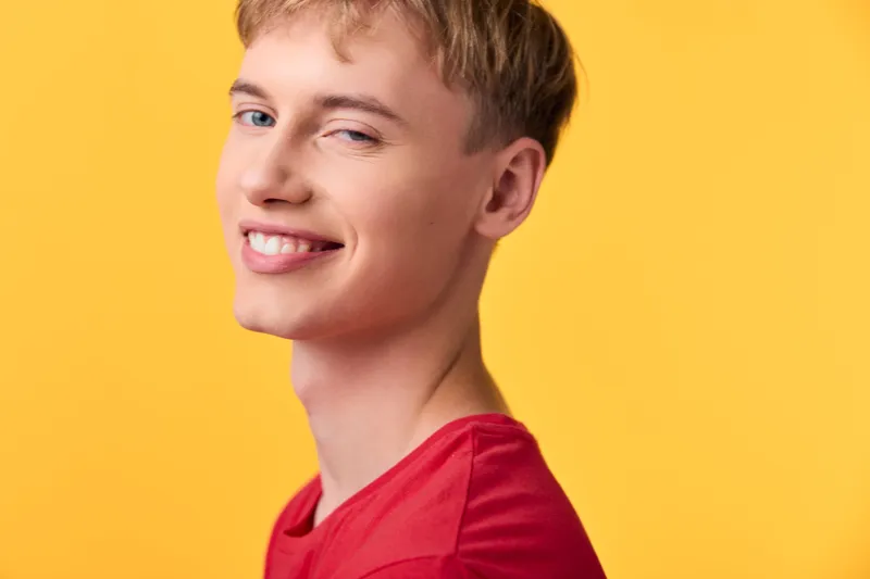 Smiling young male in a red shirt against a bright yellow background, casual lifestyle shot capturing cheerful energy, positive mood and everyday fashion for youth themes