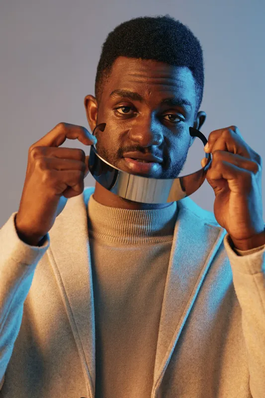 Stylish man wearing a modern collar, demonstrating confident emotions against a blue backdrop showcasing contemporary fashion trends