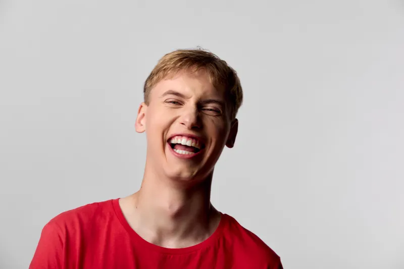 Smiling man in a red shirt bursts with laughter, capturing a moment of pure happiness and joyful energy, casual mood, expressive face and confident attitude