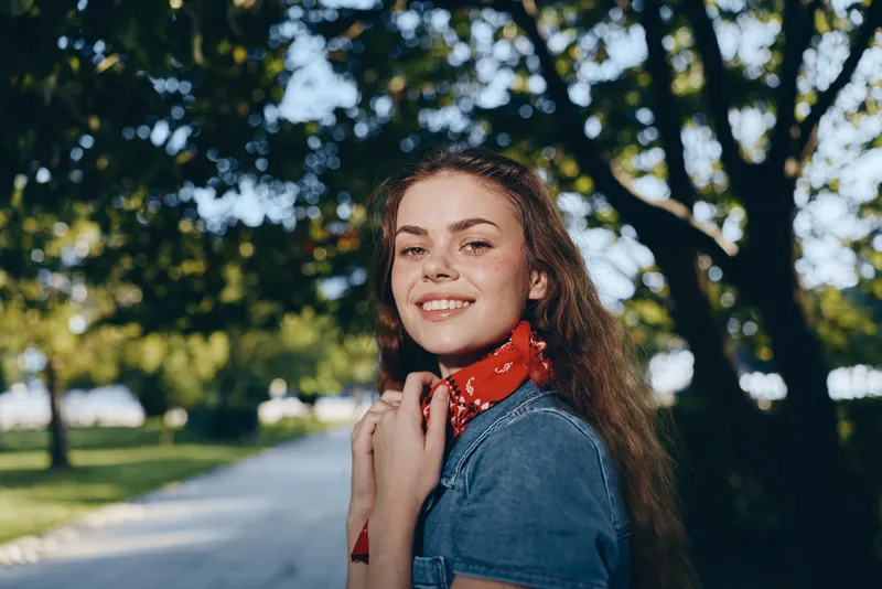 Smiling woman in modern boho-western denim street style with film color effect, outdoors in a sunny park, casual and natural atmosphere.