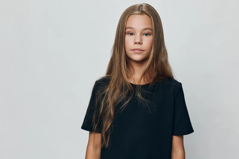 Girl with long hair in black t shirt standing with neutral expression against plain background. Portrait of child with natural look and casual clothing isolated in studio.