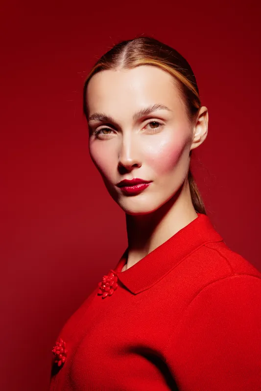 Portrait of confident woman with red lipstick and red outfit on red background. Studio lighting highlights her clear skin and sharp facial features. Fashion and beauty concept.