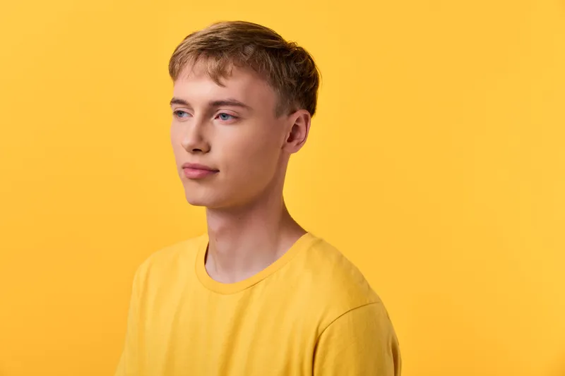 Young man in a yellow shirt against a bright studio backdrop, minimalist fashion style, calm expression, clean lighting, ideal for branding, lifestyle, or apparel campaigns, suitable for ads.