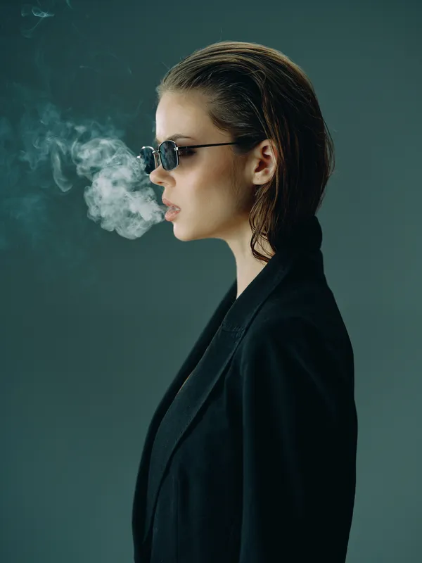 Side profile of stylish woman with sunglasses exhaling smoke wearing black coat