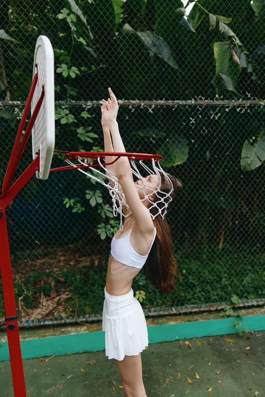Young woman in white sportswear celebrating a victory in basketball, joyful expression, outdoors with lush greenery in the background