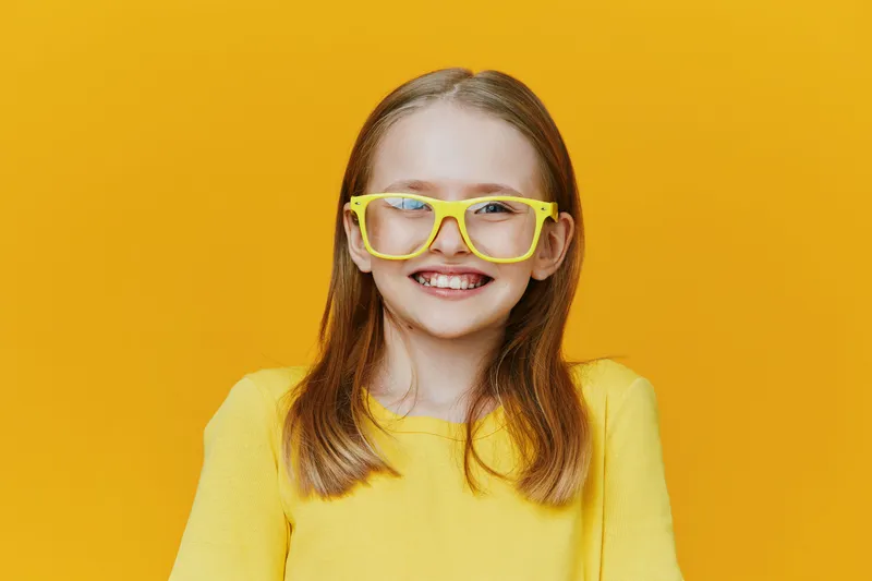 Happy young girl with glasses smiling against a bright yellow background, wearing a yellow sweater, embodying joy, creativity, and youthfulness