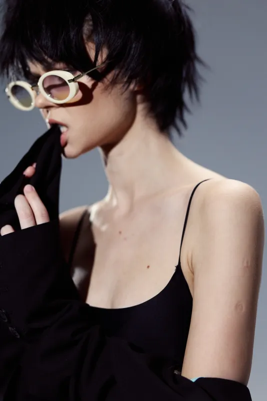 Stylish woman with short hair wearing sunglasses and black clothing in moody lighting