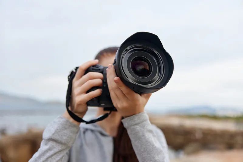 Young female photographer capturing the moment with a DSLR camera on a serene beach backdrop, showcasing creativity and passion for photography