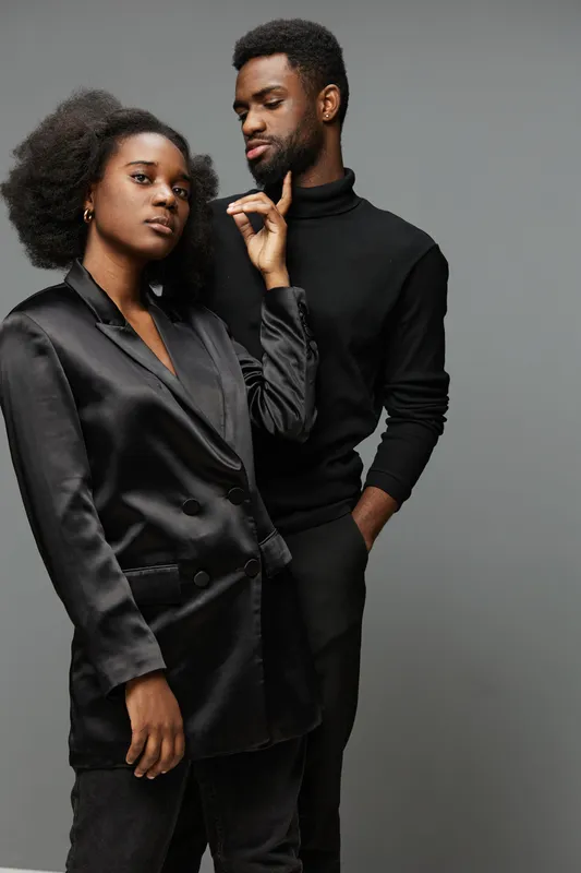 Stylish young African American couple in sleek black outfits showcasing confidence and elegance in a minimalist studio setting