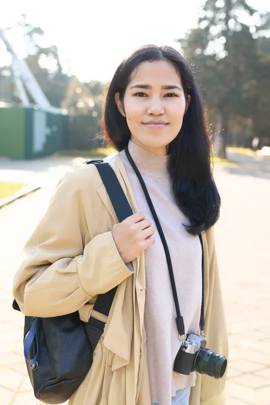 Camera, backpack, outdoor lifestyle scene featuring a casual traveler with a camera strap, daylight glow, soft sweater and jacket, relaxed pose, exploring open space in daylight.